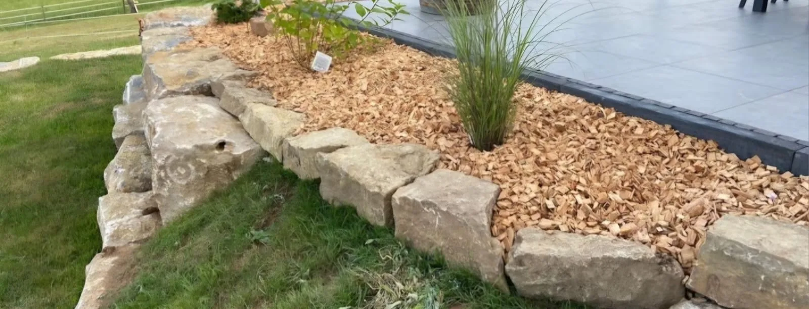 Mit Holzhackschnitzeln gemulchtes Beet entlang einer Natursteinmauer